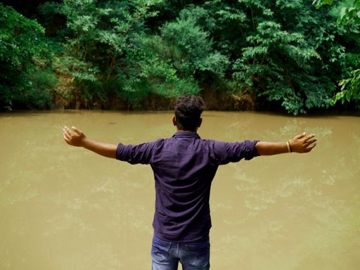 A back view of an Indian male with open arms near a river