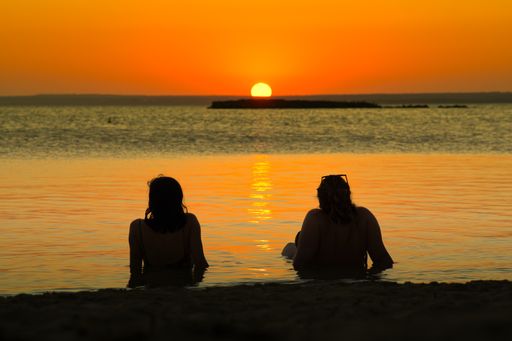 A silhouette shot of two women sitting near the water during a beautiful sunset