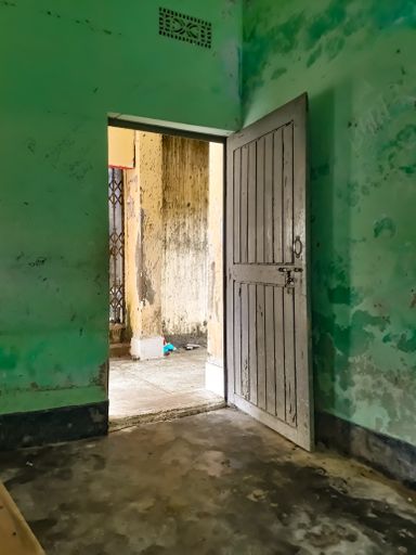 An open wooden door of an old room with green weathered walls