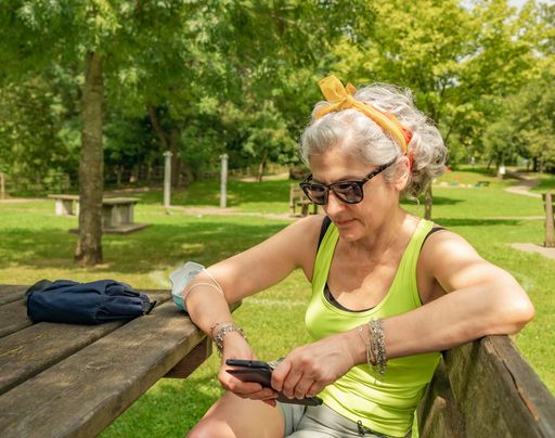 A vertical shot of the old white woman in shape looking at her phone.