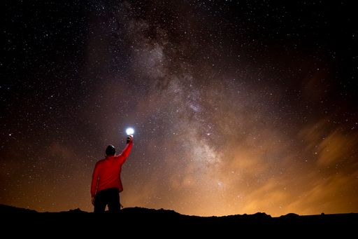 A male holding an illuminated flashlight under a galaxy starry sky
