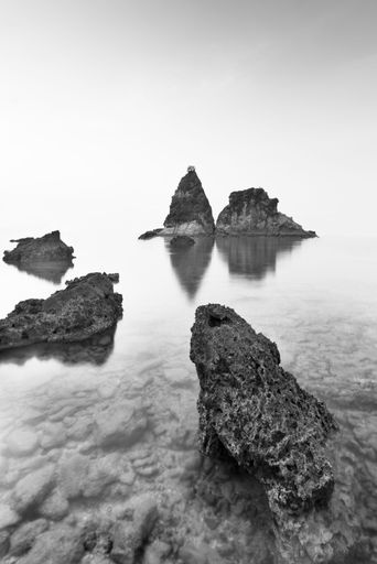 Black and white seascape with jagged rocks and calm water reflecting the sky, creating a serene and timeless atmosphere.