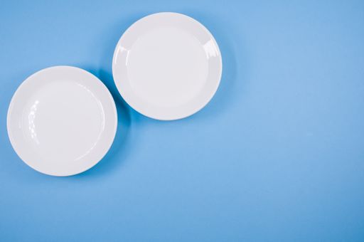 A top view of empty ceramic white plates on a blue  background