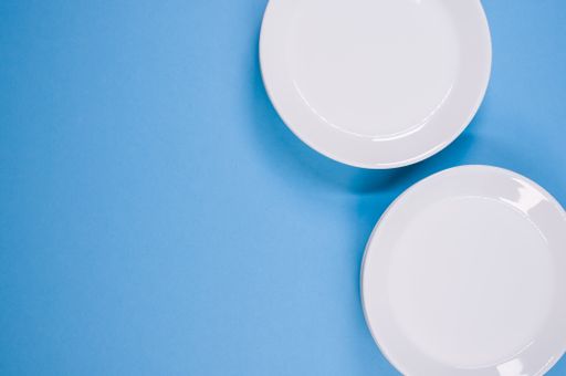 A top view of empty ceramic white plates on a blue  background