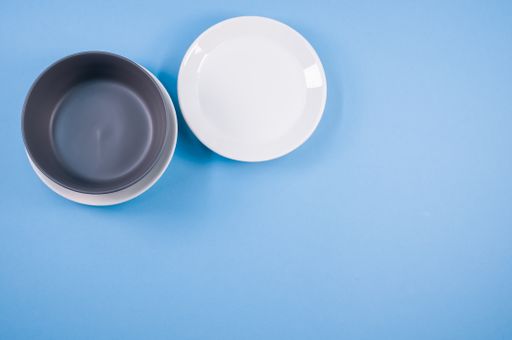 A top view of an empty ceramic white and black plates on a blue  background