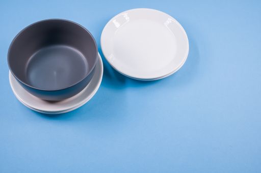 A top view of empty ceramic white and black plates on a blue  background
