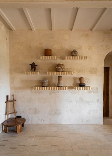 Rustic interior with textured walls, wooden chair, and decorative pottery on shelves, creating a warm and inviting atmosphere.