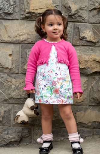 A cute Caucasian girl with ponytails, wearing a white dress and a pink jacket walking down the street