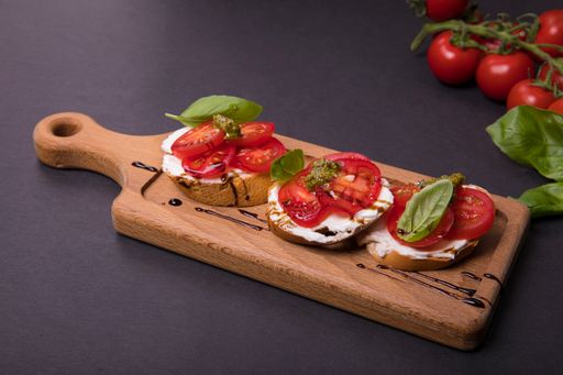 Tasty bruschetta with cherry tomatoes, pesto, basil and cheese on a wooden board