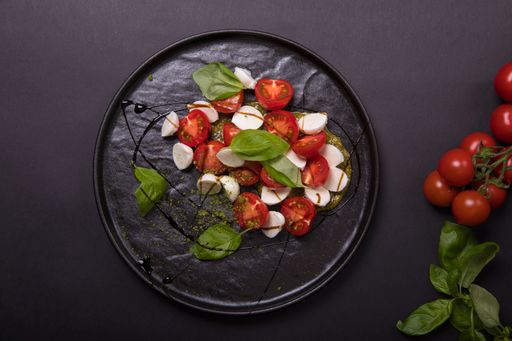 A top view of a caprese salad with basil on a tray on a black background