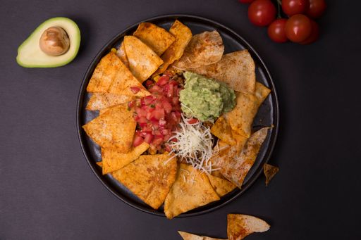 A top view of nachos with guacamole sauce, chopped tomatoes and cheese on a black background