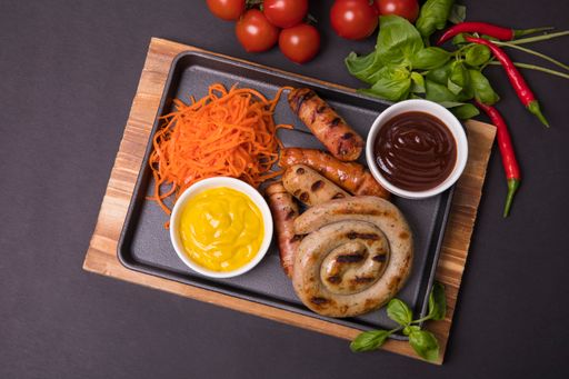 A top view of Bavarian sausages with grated carrot, vegetables and two different sauces on a tray