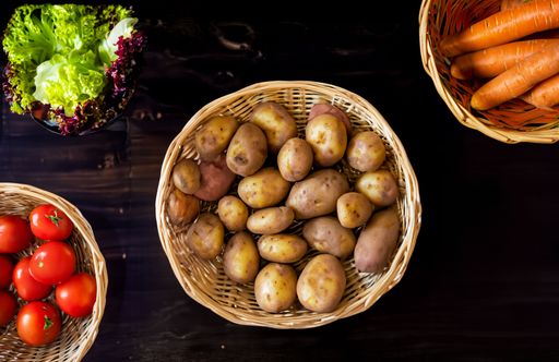 A top view of fresh vegetables including potatoes, carrots, tomatoes, and lettuce in wicker baskets