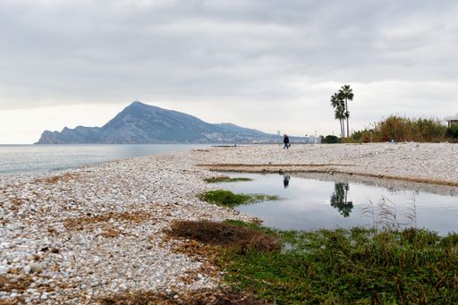 A lakeshore with stones and pebbles with a mountain and a cloudy dark sky