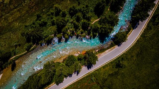 Aerial view of a winding river with lush greenery and a nearby road, showcasing nature's beauty from above.
