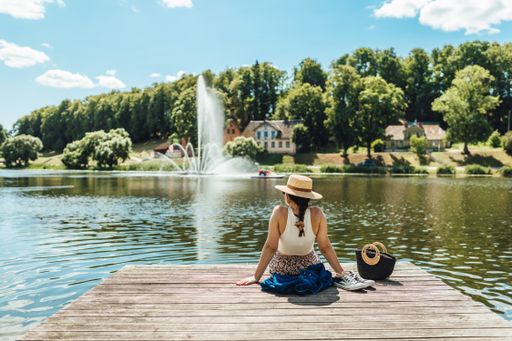 A back view of a young lady sitting on a wooden dock and leaning back on hands by a lake