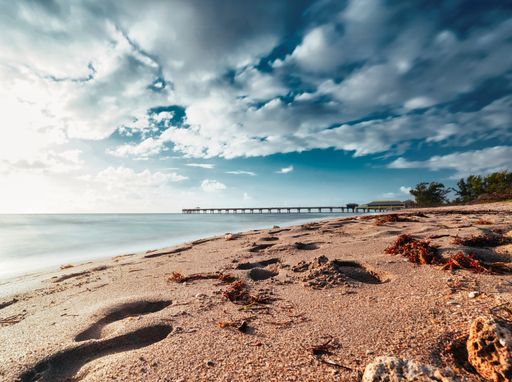 a beautiful view of sandy seashore with human footprints under cloudy sky