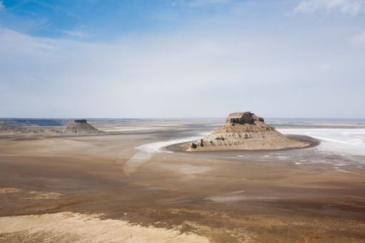Aerial view of two isolated mesas in a vast desert landscape under a clear blue sky, highlighting the stark beauty of the arid terrain.