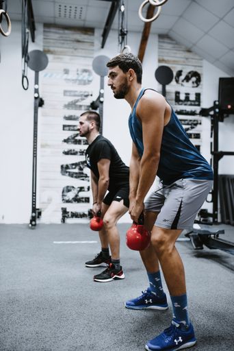 a vertical shot of two young males in sportswear working out with kettle-bells at gym