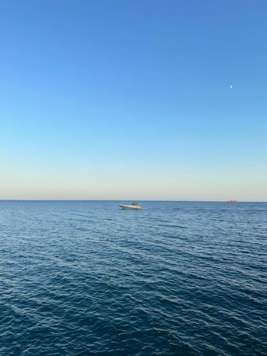 A serene seascape with a small boat on calm waters under a clear blue sky, featuring a distant ship on the horizon.
