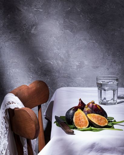 A vertical shot of figs and a glass of water on a table with a wooden chair