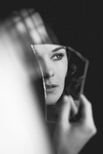 A vertical grayscale shot of an elegant European woman from Germany holding a broken piece of mirror