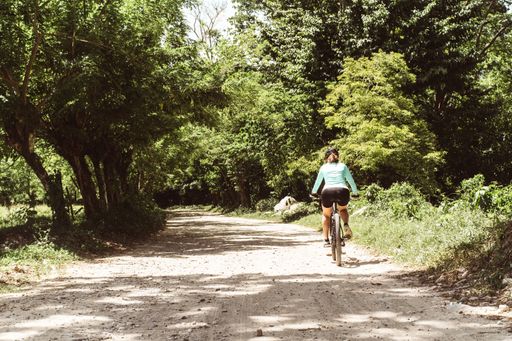 A Hispanic female cyclist in sportswear with a helmet and glasses riding a bicycle