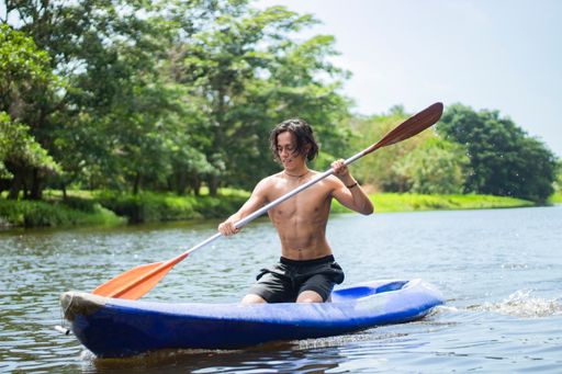 A handsome Colombian male paddling on a kayak against blurred trees