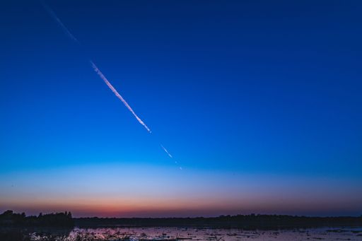 A serene twilight sky with a contrail over a calm lake, creating a peaceful and tranquil atmosphere.