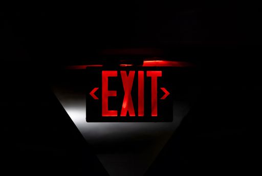 A glowing red exit sign in a dark setting, illuminated with subtle light and shadow effects