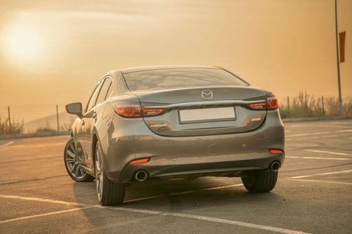 A sleek Mazda 6 sedan parked in an empty lot during sunset, showcasing its rear design under a warm golden sky.
