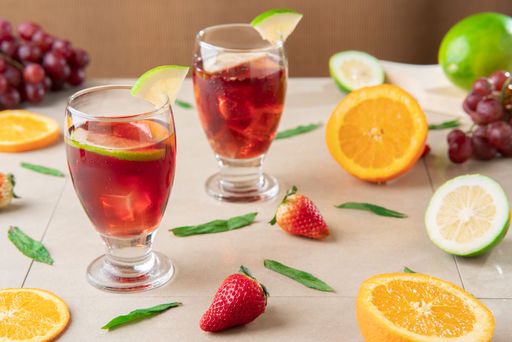 Close-up of glass cups with homemade summer wine surrounded by oranges and lemons on ceramic table