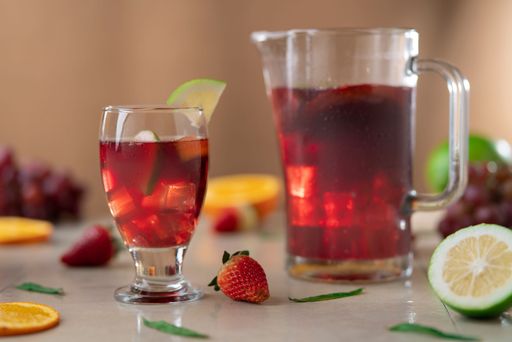 Close-up of glass and glass jug with homemade summer wine in foreground against background of oranges, strawberries and lemons on ceramic table
