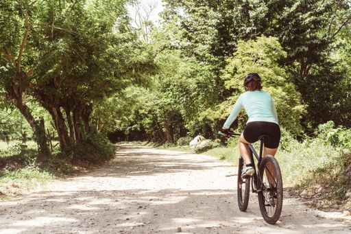 A Hispanic female cyclist in sportswear with a helmet and glasses riding a bicycle