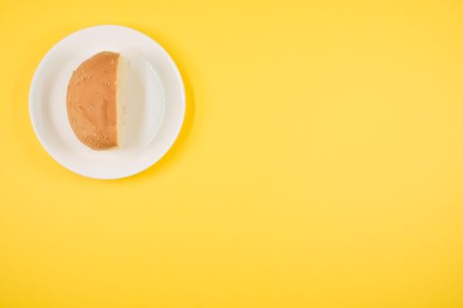 A top view of half bread bun on a plate isolated on yellow background