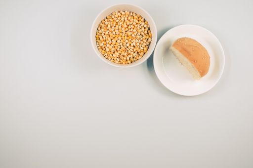 A top view of half bread bun and corn grains on a plate isolated on white background