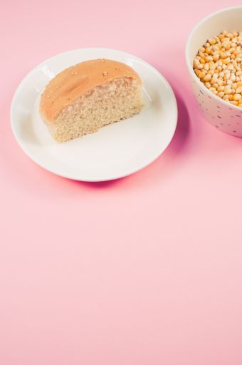 A vertical shot of half bread bun and corn grains on a plate isolated on pink background