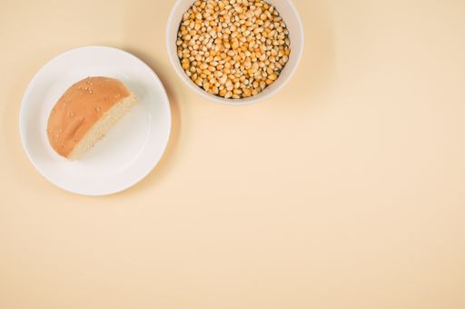 A top view shot of corn and half bread on a coral background