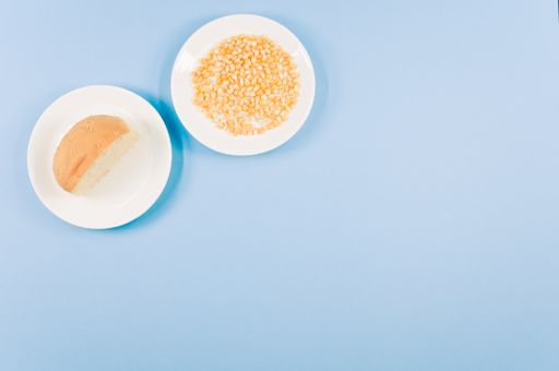 A top view of half bread bun and corn grains on a plate isolated on blue background