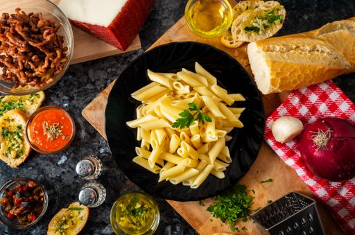 A high angle shot of a plate of pasta and uncooked ingredients on a wooden surface