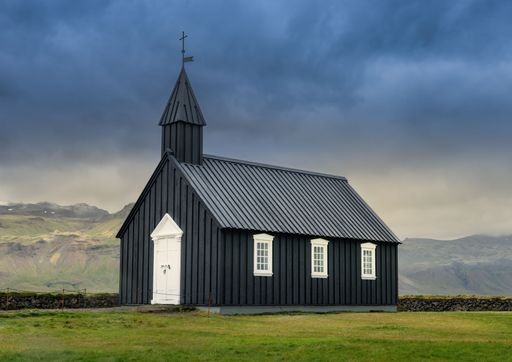 A picturesque black church set against a dramatic sky in Icelandic landscape, showcasing architectural beauty and natural scenery.