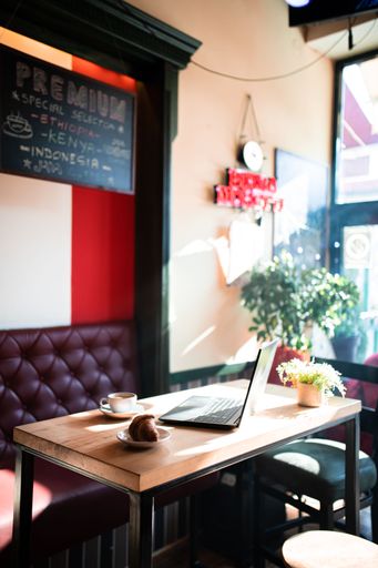 Cozy cafe corner with a laptop, coffee, and croissant on a sunlit table, perfect for remote work or relaxation.