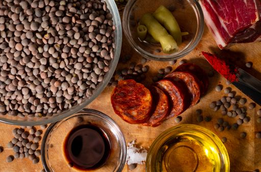 A high angle shot of a bowl of lentils, oil, and some ingredients on a wooden surface