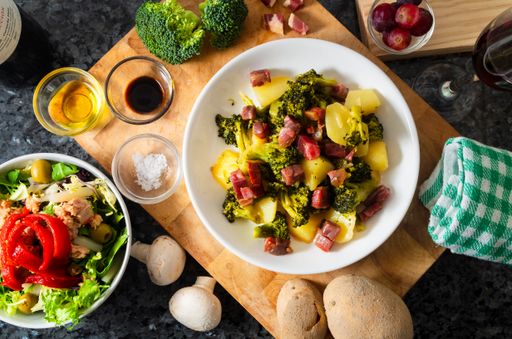 A high angle shot of a plate of fresh potato salad and some ingredients on a wooden surfa