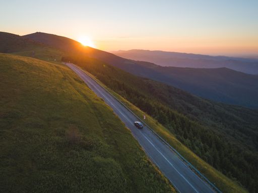 An aerial shot of a vehicle on the road on a rural hill during sunset
