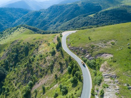 An aerial shot of a vehicle on the road on a rural hill surrounded by plants