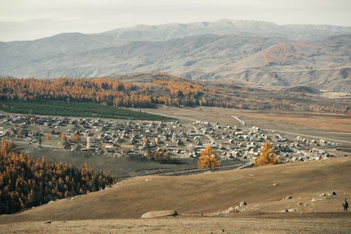 Scenic view of a rural village nestled in a valley surrounded by autumnal forests and mountains under a clear sky.