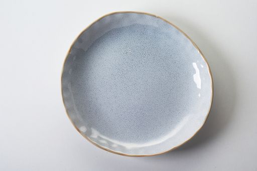 A top view of a new light gray ceramic plate with a relief pattern and golden rim on white background