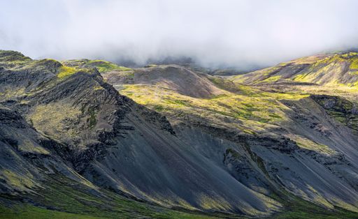 Scenic view of a rugged mountain landscape with vibrant green patches under a cloudy sky, showcasing natural beauty and tranquility.