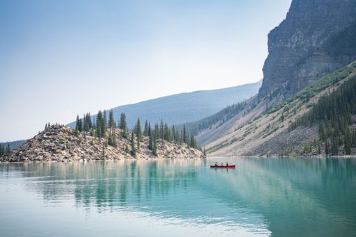 Serene lake scene with a red canoe and forested mountains in Banff National Park, Alberta, Canada under a clear blue sky.